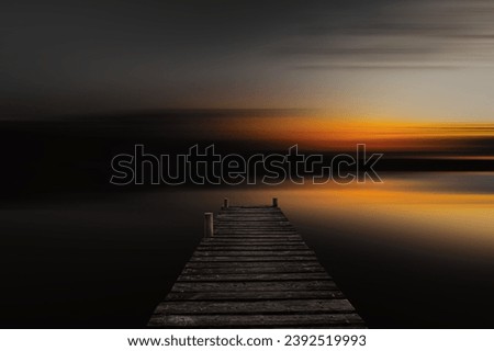 Old wooden boardwalk, dock in lake with abstract blurred background in dark evening. Abstract blurred sunset background.