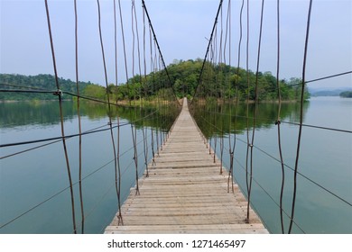 Old wooden bridge hanging with rope is a long line pass to a small island at the other side of the lake. Natural park view. Lake with blue sky.