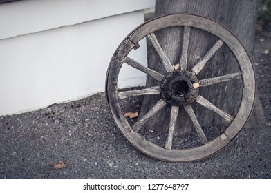 An Old Wooden Cartwheel Stands At The Wall Of The House.