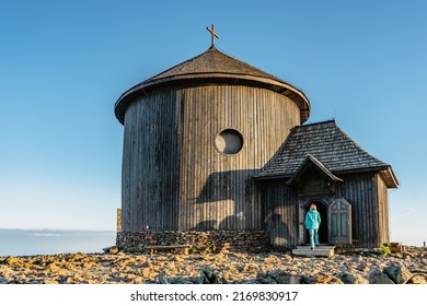 Old wooden church on the top of Snezka,the highest mountain of Czech Republic,Krkonose Mountains. Girl in blue jacket walking to chapel of Saint Lawrence.Hiking to the summit.Sunny day in countryside.
