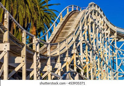 An old wooden construction rollercoaster against a blue sky and palm tree