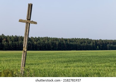 An Old Wooden Cross In A Field, A Field With A Grain Harvest And A Wooden Religious Cross