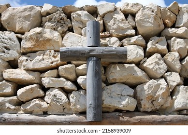 An Old Wooden Cross Fixed On A Stone Wall.