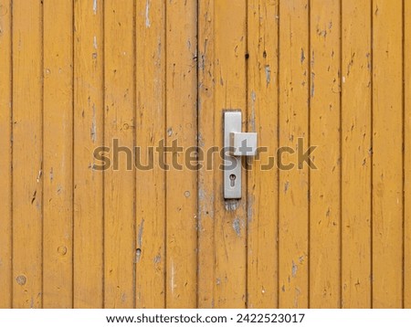 Old wooden door with an old filthy knob. The entrance is weathered and aged. The exterior paint is peeling off and dirt stains are on the facade. Close up of an old fashioned building wall.