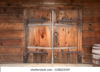 Old Wooden Double Doors With Rusty Weathered Hardware, Wooden Barrels Stacked Beside Door. Close Up.