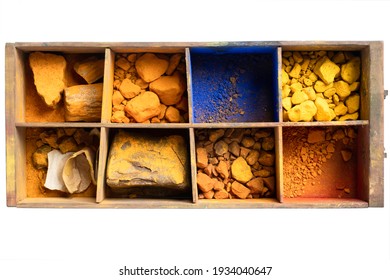 alte Holzschublade mit Fächern, die blaue, gelbe und orangefarbene Pigmente und getrocknete Farbstoffe enthalten, die mit Öl für einen Maler auf weißem Hintergrund gemischt werden