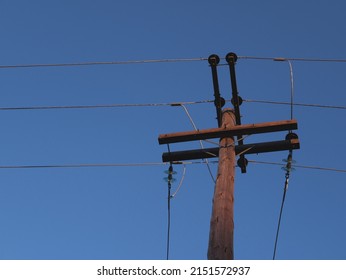 An old wooden electric pole against the cloudless sky