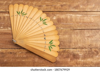 An old wooden fan lies on a wooden background.