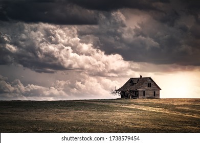 Old wooden farmhouse in the countryside at sunset with storm  clouds in the sky. There is a short grass meadow around the house.