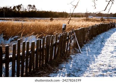 An old wooden fence overgrown with moss in a snowy field with dry yellow grass in early spring. Rural landscape - Powered by Shutterstock