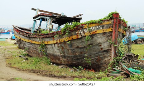 An old wooden fishing boat sits abandoned on a beach in Vietnam, with plant-life slowly creeping up the battered hull