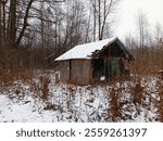 Old wooden house in the middle of the forest in winter with traces of destruction on the background of snow. Small house and shelter in the forest. Winter landscape in the forest with a forester