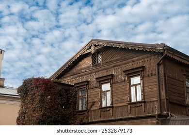 Old wooden house with ornate woodwork and autumn ivy, set against a backdrop of fluffy clouds. Ideal for architectural heritage, cultural tourism, or autumnal themes - Powered by Shutterstock