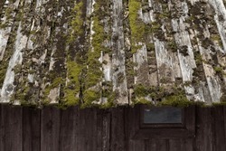Old Wooden House Roof With Green Moss And Wall Made Of Rough Gray Boards, Background Photo Texture
