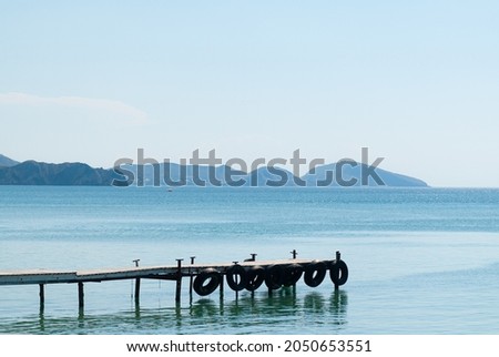 an old wooden long pier with tires hanging on the sides against the background of distant rocks and the blue sea