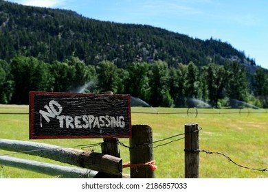 An old wooden No Trespassing sign made with black and red paint attached to a wooden fence post. 
