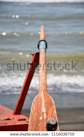 An old wooden oar rests in its rowlock pointing at the sea