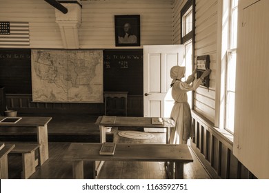 Old Wooden One Room School House In Rural America And Woman In Traditional Period Dress With Bonnet In Sepia Tone. 