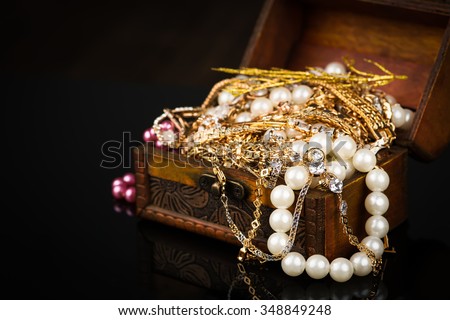 Old wooden open chest with golden jewelry on black background