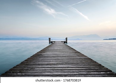 An old wooden pier extends into the clear blue waters of the lake. A solitary path towards the calm and peaceful silence of nature, with the sweet sound of the waves. - Powered by Shutterstock