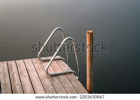 Old wooden pier with ladders to a lake. Autumn sunrise and foggy lake.