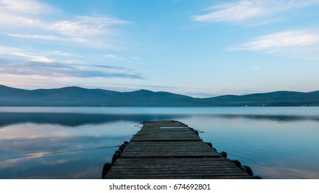 Old Wooden pier on the lake. Long exposure. Landscape view with wood bridge in Lake and Mountain background. Wooden pier on the lake. Sunset in pastel colors.  - Powered by Shutterstock