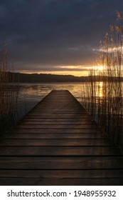 An Old Wooden Pier On The Shore Of The Lake Sempachersee At Dusk In The Golden Light. Clouds In The Sky And Reeds In The Water - Image