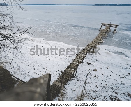 An old wooden pier in winter on a frozen lake goes into the distance, a wooden pier construction in winter