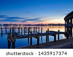 Old wooden piers stand empty in the still waters of the Severn River at twilight. Colorful skies on the horizon at dusk, along with the evening lights of the Naval Academy and Annapolis, Maryland.