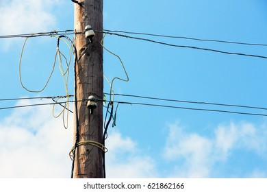 Old wooden pillar with power line against the blue sky. A botched electrical connections