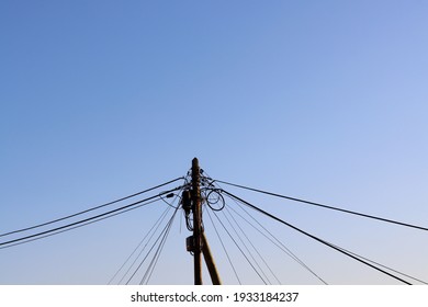 Old Wooden Pole, With A Wiring Harness, Power Lines, Telephone, Cable TV Against A Blue Sky. A Mess Of Wires On A Pole