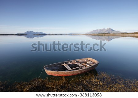 Old wooden rowing boat at Norwegian coast at clear sunny day, with mountains at horizon. Photographed at Helgeland, Nordland, Norway. 