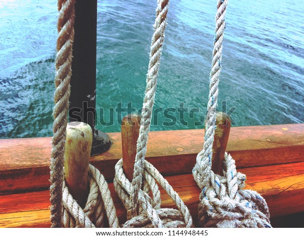 Old wooden sailboat\'s ropes tied off for\
sails with water in\
background.