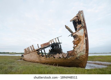 An old wooden shipwreck, showing signs of decay and deterioration. An old nauitical sea vessel grounded on the shore with rusty rotten ruins. Nature and the sea taking its toll on old boats.