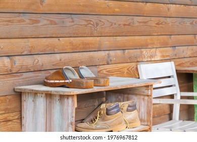 Old Wooden Shoebox Near A Wooden Cottage On A Farm. The Shoe Box Has Old Clogs, Rubber Boots And Shoes.