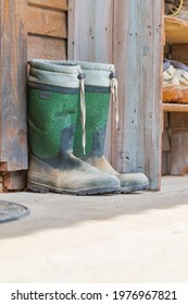 Old Wooden Shoebox Near A Wooden Cottage On A Farm. The Shoe Box Has Old Clogs, Rubber Boots And Shoes.