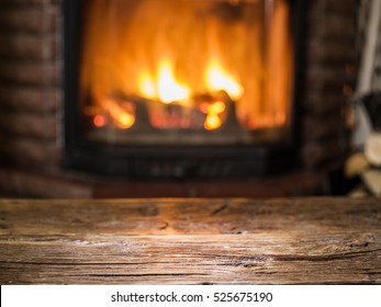 Old Wooden Table And Fireplace With Warm Fire On The Background.