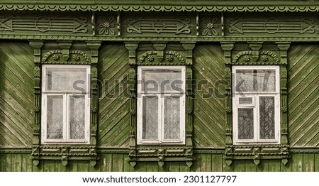 Old wooden windows with carved green architraves on green painted, sheathed with wooden slats facade of typical rural house. Nizhny Novgorod region, Russia. Architecture concept.
