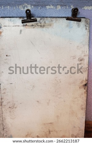 Old worn drawing board with two rusty metal binder clips, mounted against a faded pastel textured wall.