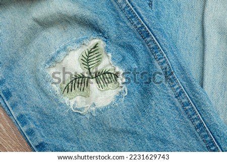 Old worn jeans with a patch sewn in place of a hole.Mending clothes concept.Reusing old jeans.Sustainable fashion, 