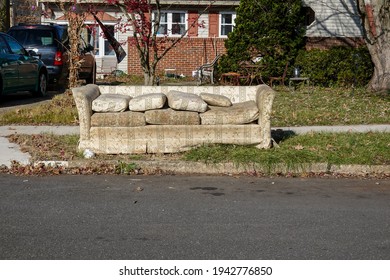 Old Worn Out Couch By The Curb Waiting For Trash Pickup In Front Of An Old House With A Messy Yard On A Sunny Day