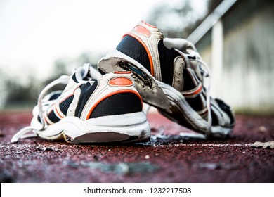 Old Worn Out Running Shoes With Holes On Red Running Track