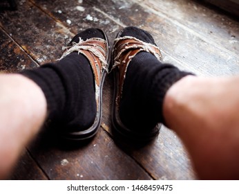 Old Worn Out Sandals Thread Bare With Black Socks Against A Worn Wooden Floor