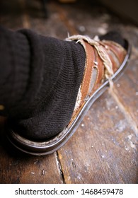 Old Worn Out Sandals Thread Bare With Black Socks Against A Worn Wooden Floor