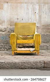 Old Worn Out Yellow Chair Against A Stone Wall 