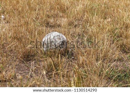 Old worn shabby and torn soccer ball on field of rural abandoned stadium. Rubbed, worn, torn with hole spoiled leather ball on old wiped well-groomed stadium. Old leather ball on grass