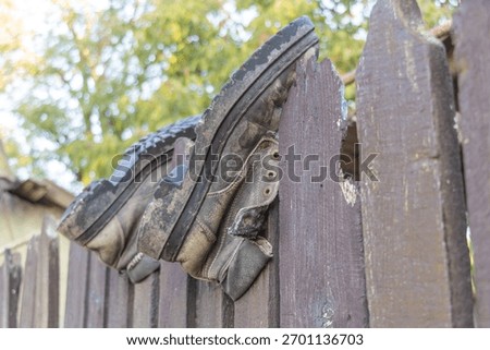 Old worn work boots hanging on a wooden fence outdoors, symbolizing rural lifestyle and hard labor background