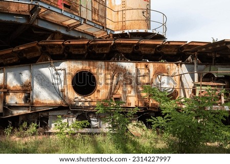An old and worn-out bucket wheel excavator with a variety of metallic parts scattered across its surrounding area