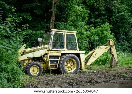 Old yellow backhoe loader parked at forest edge with overgrown vegetation