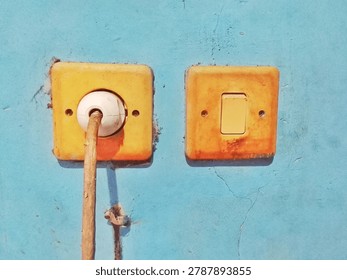 Old Yellow Electrical Socket with Plug and Switch Mounted on Weathered Blue Wall